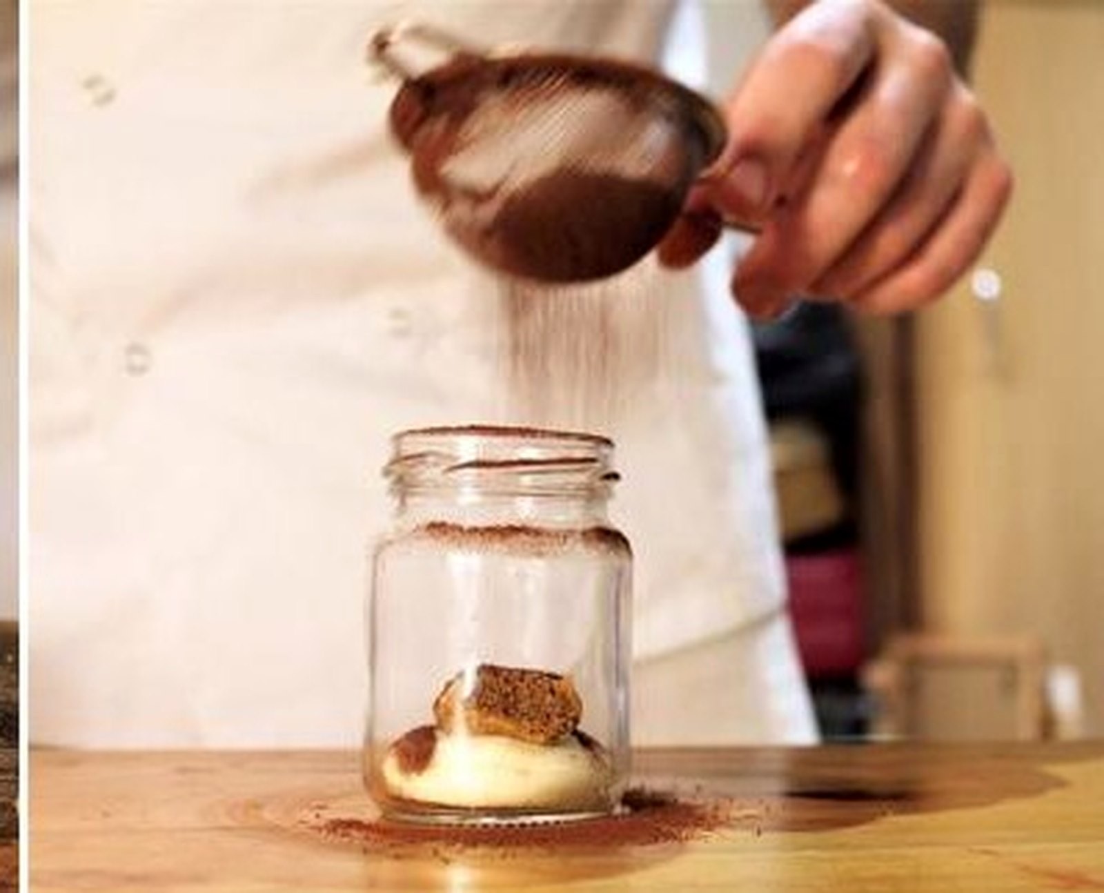 A jar of Coccole tiramisù being finished with a dusting of cocoa
